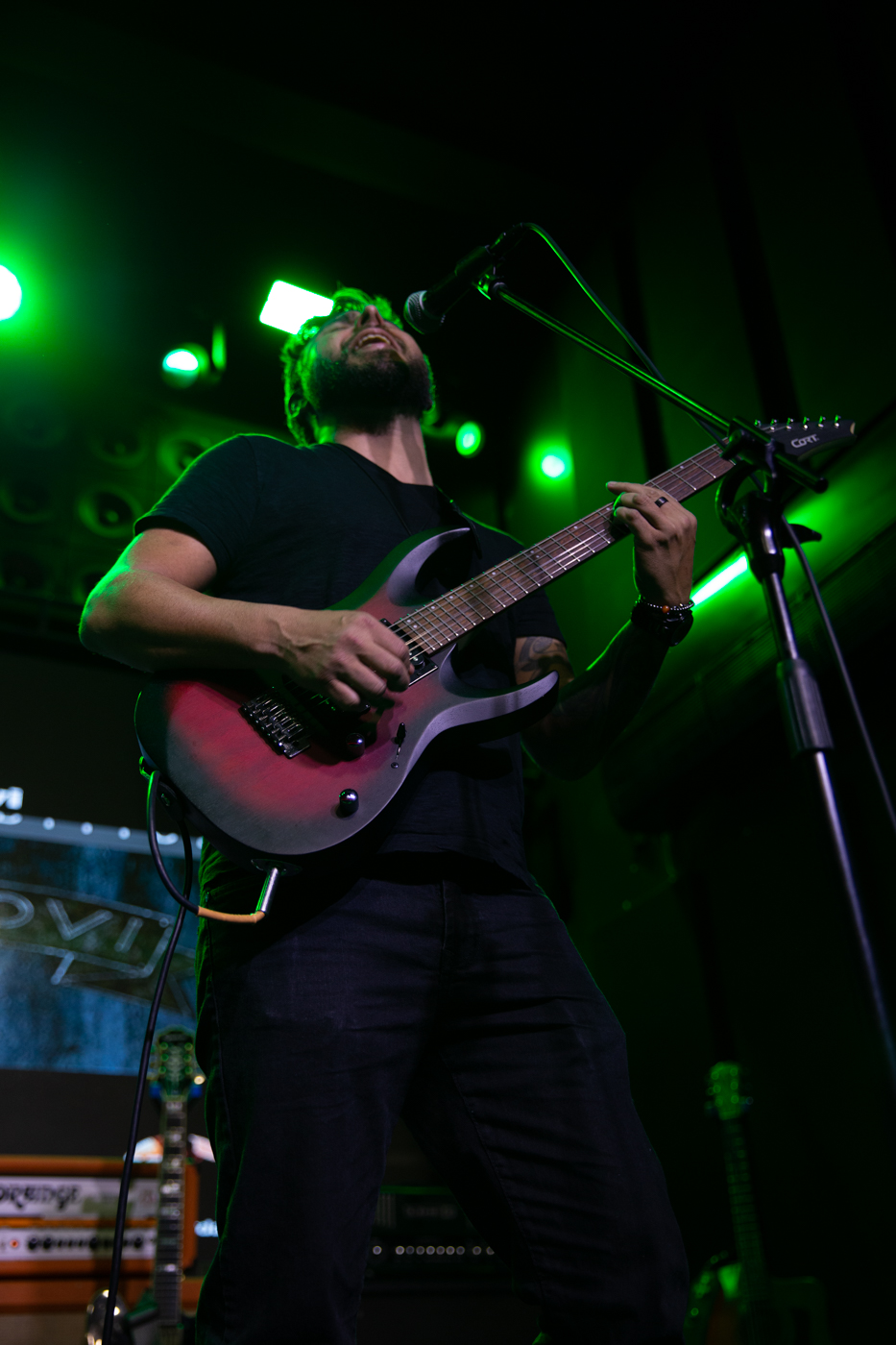 Guitarrista e vocal do Bunkers ao vivo, com guitarra avermelhada sob luz verde de palco