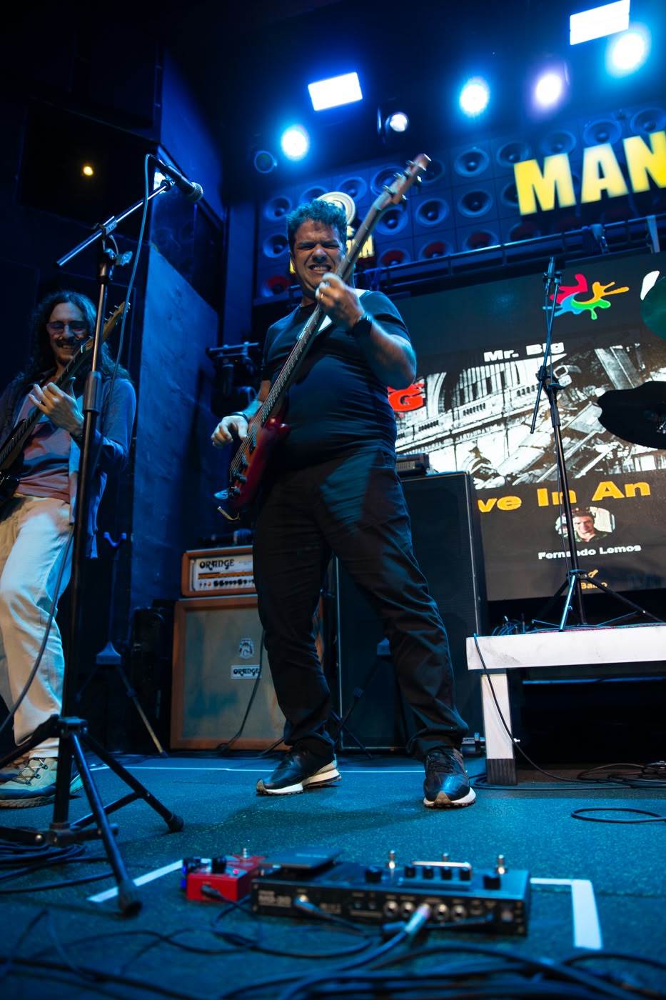 Baixista do Bunkers ao vivo durante Mr. Big, com painel de LED e amplificadores ao fundo