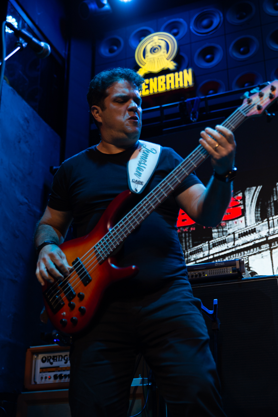 Baixista do Bunkers ao vivo, com baixo de 5 cordas sob luz azul de palco